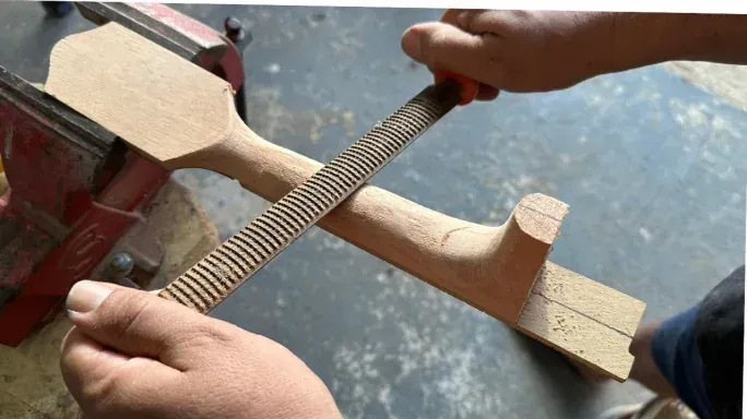 Mãos lixando o braço do instrumento preso na morsa
